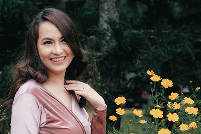 Thoughtful woman smiling while standing by orange flowers outdoors