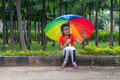 Full length of girl with umbrella sitting in rain