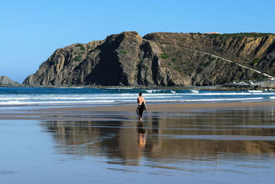 Man standing on rock by sea against clear sky