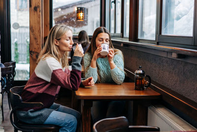 Two lovely women drink tea in a bar at a table by the window.