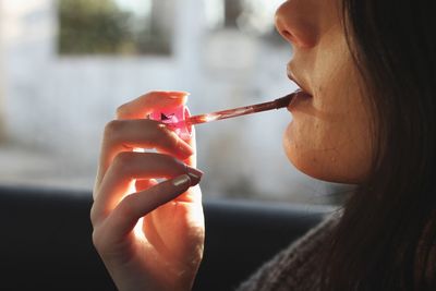 Midsection of young woman applying lip gloss in car