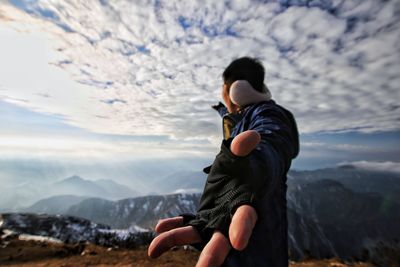 Woman holding hands against cloudy sky