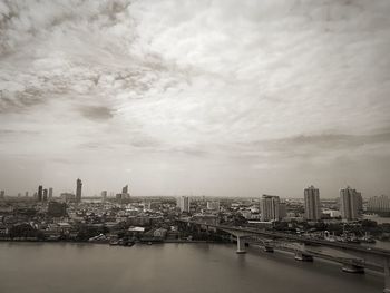 View of city at waterfront against cloudy sky