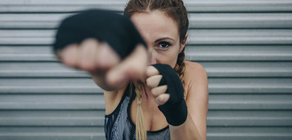 Young sportswoman with boxing bandages looking at camera and punching. focus on face in background