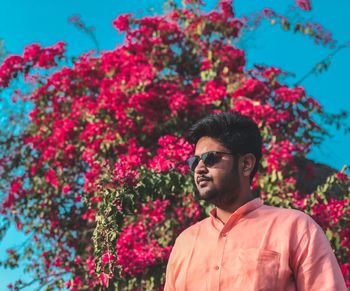 Young man wearing sunglasses standing by pink flowering plants