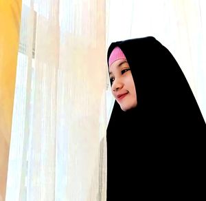 Portrait of smiling young woman standing against curtain