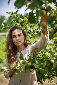 Portrait of woman picking fruit from tree