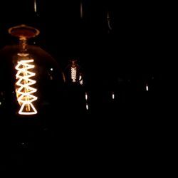 Close-up of illuminated light bulb hanging in the dark