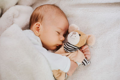 High angle view of cute baby boy sleeping with stuffed toy on bed at home