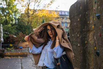 Portrait of young woman wearing jacket in city during rain