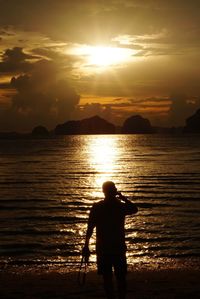Silhouette man standing at beach against sky during sunset