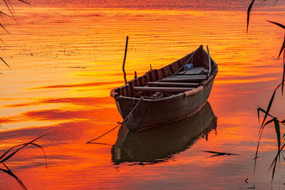 Boat moored on sea against orange sky