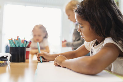 Girl using felt tip pen in drawing class with classmates in background