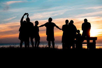 Silhouette people on beach against sky during sunset