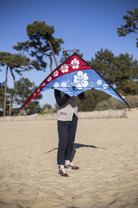 Woman with kite standing at beach against clear sky