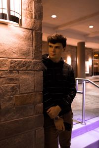 Young man standing against illuminated wall at night