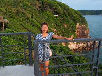 Portrait of smiling young woman standing against railing