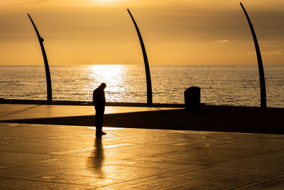 Silhouette man standing by sea against sky during sunset