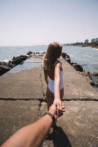 Rear view of woman holding hand of boyfriend by sea on pier