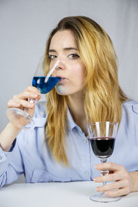 Portrait of young woman having drink in wineglasses against backdrop