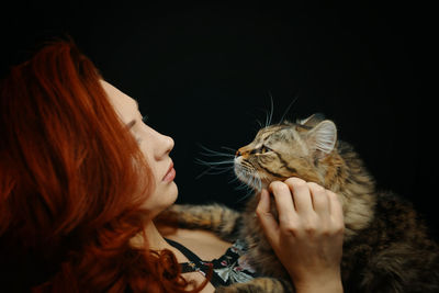 Midsection of woman holding cat against black background