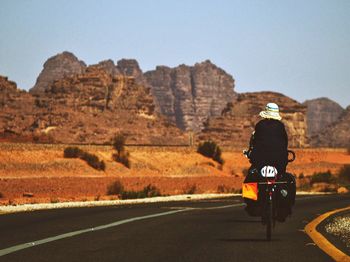 Person bicycling on road against rocky mountains