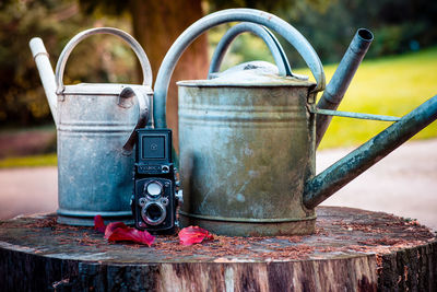 Close-up of old watering cans with camera on tree stump