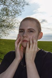 Portrait of beautiful young woman, hands on the face, against sky