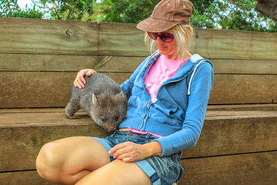 Woman sitting with wombat at bench