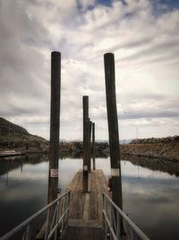 Wooden posts on pier over lake against sky