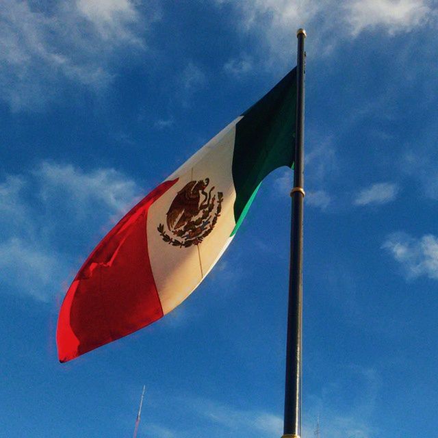 low angle view, flag, patriotism, identity, sky, national flag, american flag, pole, blue, cloud, cloud - sky, flag pole, culture, wind, day, multi colored, striped, no people, outdoors, pride