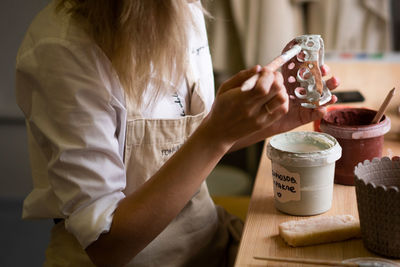 Close up view of female potter wearing apron using glaze brush to paint on pot