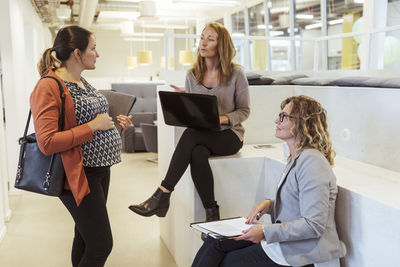 Businesswoman with laptop talking to pregnant colleague in office