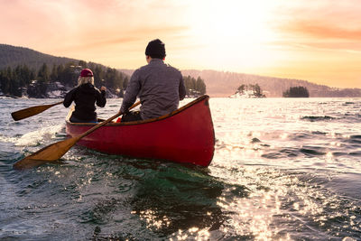 Rear view of men on boat against sky during sunset