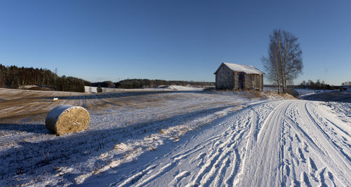 Hay bale and farmhouse in snow covered field