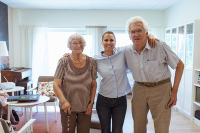 Portrait of smiling young woman with grandparents standing together in nursing home