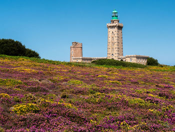 View of lighthouse by building against clear blue sky