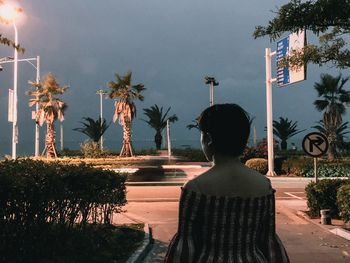 Rear view of woman standing by palm trees against sky