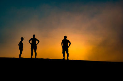 Silhouette friends standing on field against sky during sunset