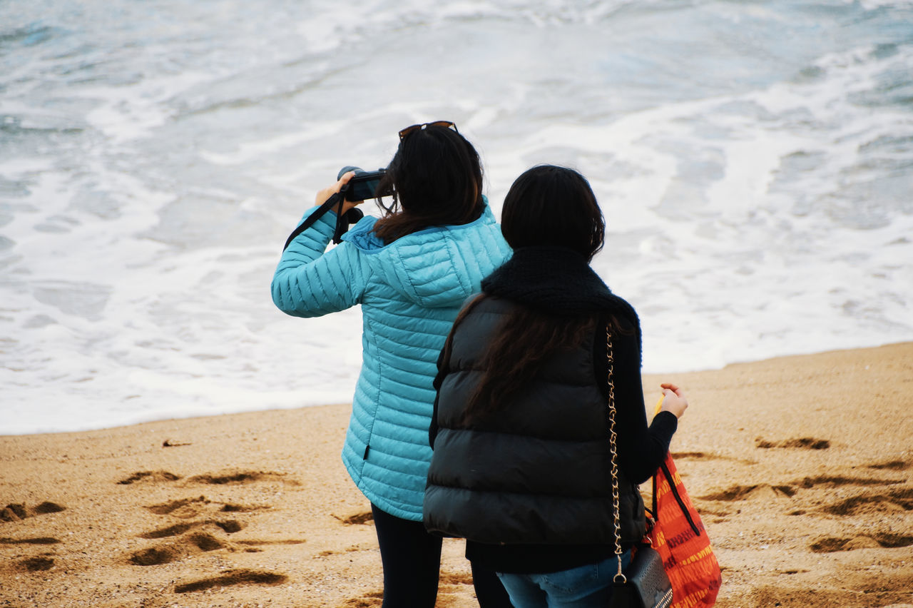 REAR VIEW OF WOMAN PHOTOGRAPHING ON SAND