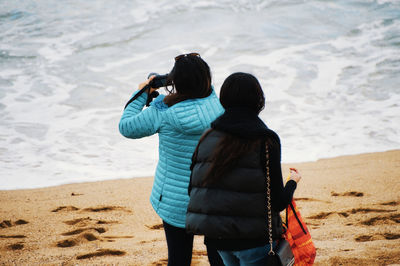 Rear view of woman photographing on beach