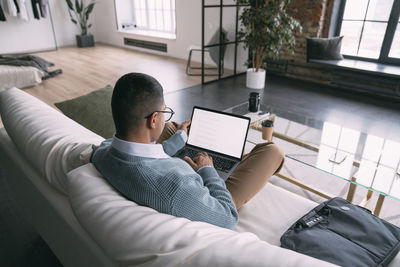 Freelancer using laptop sitting on sofa in living room at home