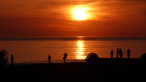 Silhouette people on beach against orange sky