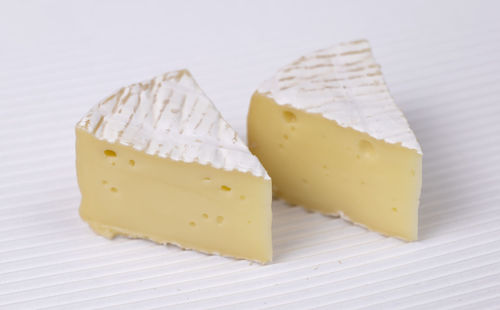 Two slice of round brie cheese out over white corrugated background, close up view.