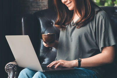 Midsection of businesswoman with laptop having coffee while sitting on armchair