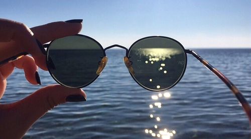 Close-up of hand holding sunglasses at beach against sky