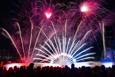 Crowd against firework display in sky at night