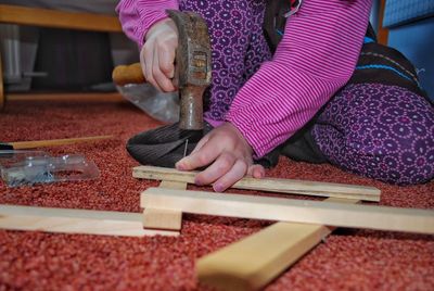 Midsection of girl hitting nail in wooden plank with hammer at home