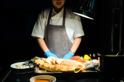 Midsection of chef preparing food in dark kitchen