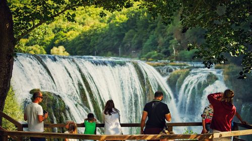 People standing by river against trees